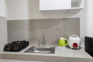 A kitchen with a sink, a kettle, a rice cooker, and a black appliance with gold detailing. - Simply Homey Studio at Vida View Apartment (Makassar)