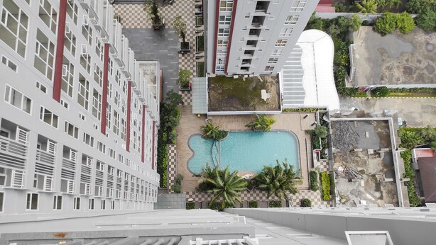 An aerial view of a residential building with a swimming pool, palm trees, and a checkered pavement area. - Simply Homey Studio at Vida View Apartment (Makassar)