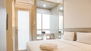 A hotel room with a bed, a desk with a chair, and a large window. - Stunning Studio at Ciputra World 2 Apartment (Jakarta)