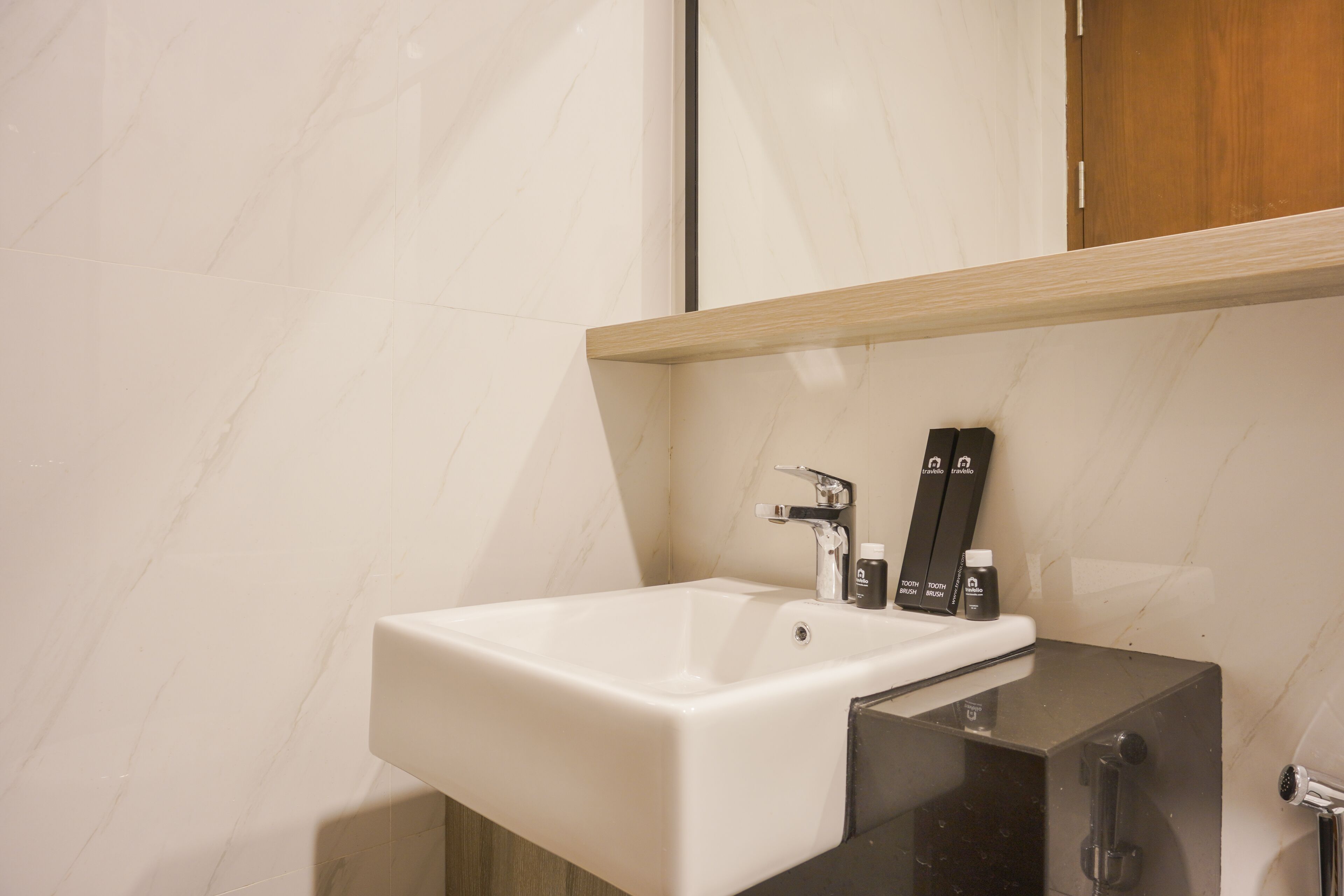 A bathroom with a white sink, a mirror, and a wooden shelf above it.
