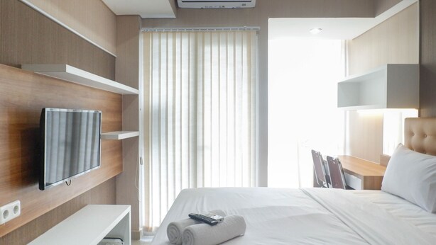 Una habitación de hotel con una cama, televisor montado en la pared, escritorio y ventana con persianas.
