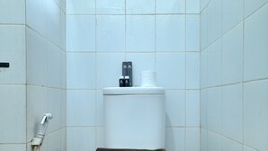 Eine weiße Toilette mit einem braunen Handtuch auf dem Sitz, einem Toilettenpapierhalter und einem Handtrockner an der Wand.