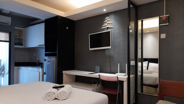 Ein Hotelzimmer mit Bett, Schreibtisch mit Stuhl, Flachbildfernseher, Spiegel und einer Küchenzeile mit Kühlschrank und Spüle.