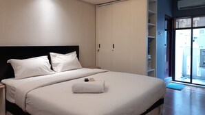 Ein modernes Hotelzimmer mit einem großen Bett, einem Nachttisch, einem Kleiderschrank und Blick durch eine Glastür nach draußen.