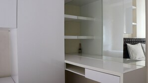 A modern, minimalist room with a large mirror, white shelving, and a bed with a grey headboard.
