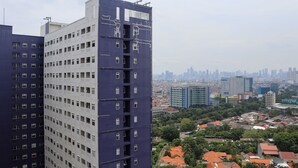 A high-rise building with multiple floors and balconies, surrounded by a cityscape with various buildings and greenery.
