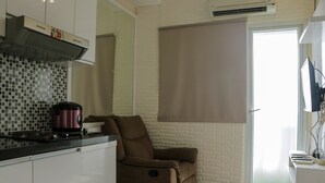 A compact kitchen with a microwave, a coffee maker, and a built-in oven. There is a sliding door with a window, and a brown recliner is positioned near the door.