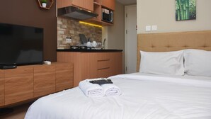 Habitación de hotel con cama, televisión, armarios de madera, microondas y un cuadro en la pared.