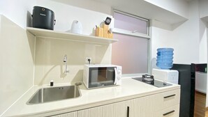 A modern kitchen with a microwave, kettle, and kettle on a shelf. There is a sink and a window above the counter. - Modern and Well Furnished 2BR at Jarrdin near Cihampelas Walk (Bandung)