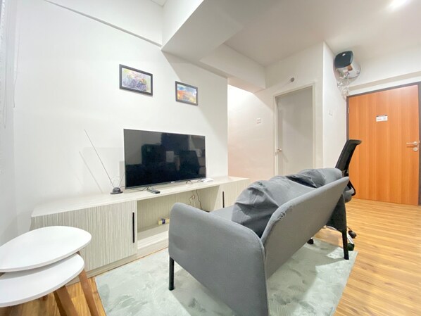 Un salon moderne avec un téléviseur à écran plat, un canapé gris, une petite table blanche et un plancher en bois.