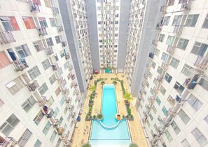 Un immeuble résidentiel de grande hauteur doté d’une piscine centrale, entourée de verdure et de balcons.