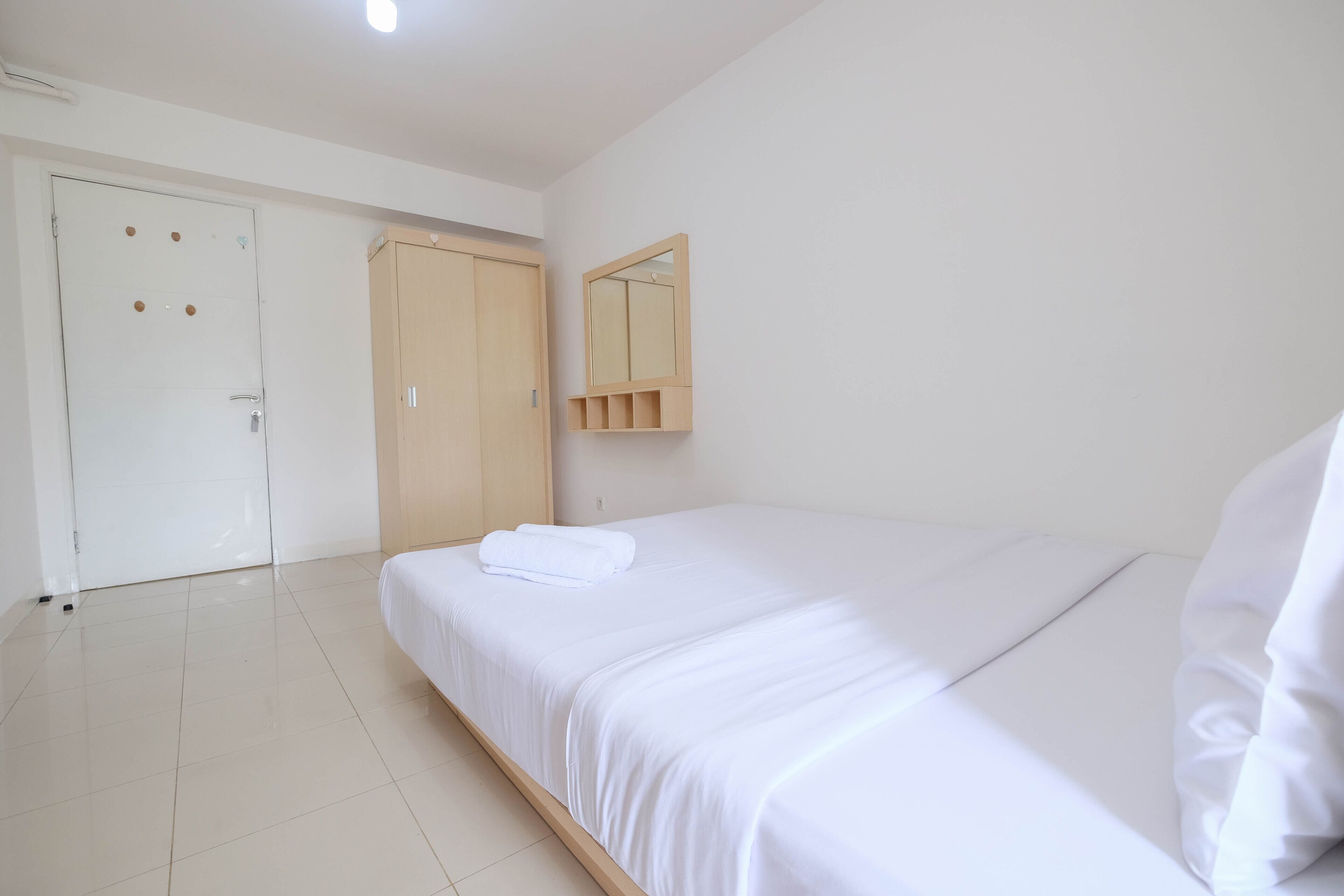 A clean, minimalist bedroom with a single bed, a wooden wardrobe, and a mirror on the wall.
