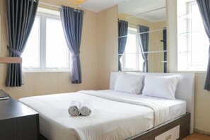 A neatly made bed with white linens, a bedside table with a remote control, and a large mirror on the wall. - Lavish 3BR Residence at Grand Palace Kemayoran (Jakarta)