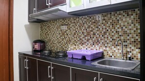 A kitchen with dark cabinets, a gas stove, a purple container, and a tiled backsplash. - Lavish 3BR Residence at Grand Palace Kemayoran (Jakarta)