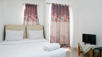 A bedroom with a bed, curtains, a TV on a table, and a chair.