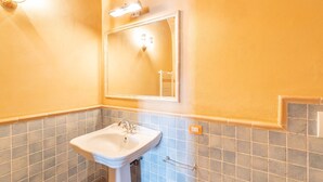 Une salle de bain avec un lavabo blanc, un miroir et un luminaire placé au-dessus du miroir.