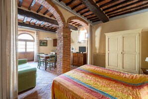 A bedroom with a bed, a dresser, and a window. There is a dining area with a table and chairs visible through an archway. - The Little Green House on Via Fonte Vecchia (Casciana Terme)
