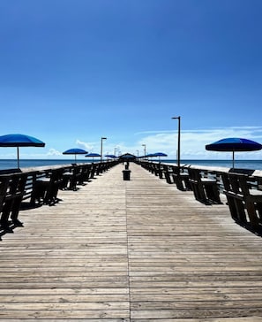 A wooden pier leading to the sea with blue umbrellas and benches. - Last minute deals for Labor Day Weekend! (Garden City Beach)