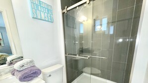 A bathroom with a glass-enclosed shower, a toilet, and a sink with towels.