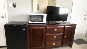 A compact kitchenette with a microwave, a small refrigerator, and a flat-screen TV on a wooden cabinet.