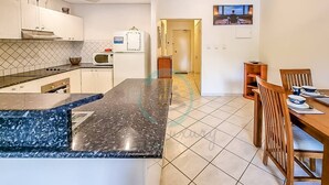 A modern kitchen with a granite countertop, white cabinets, and a dining area with wooden chairs and a table. - Zen City Balcony ~ Outdoor Dining ~ Mindal Markets (Larrakeyah)