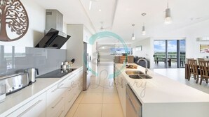 Cozinha moderna com armários brancos, ilha central com pia e luminárias pendentes.