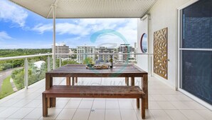 Varanda com mesa e banco de madeira, com vista para uma área residencial e vários edifícios.