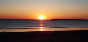 Un atardecer sobre un mar tranquilo con una costa lejana.