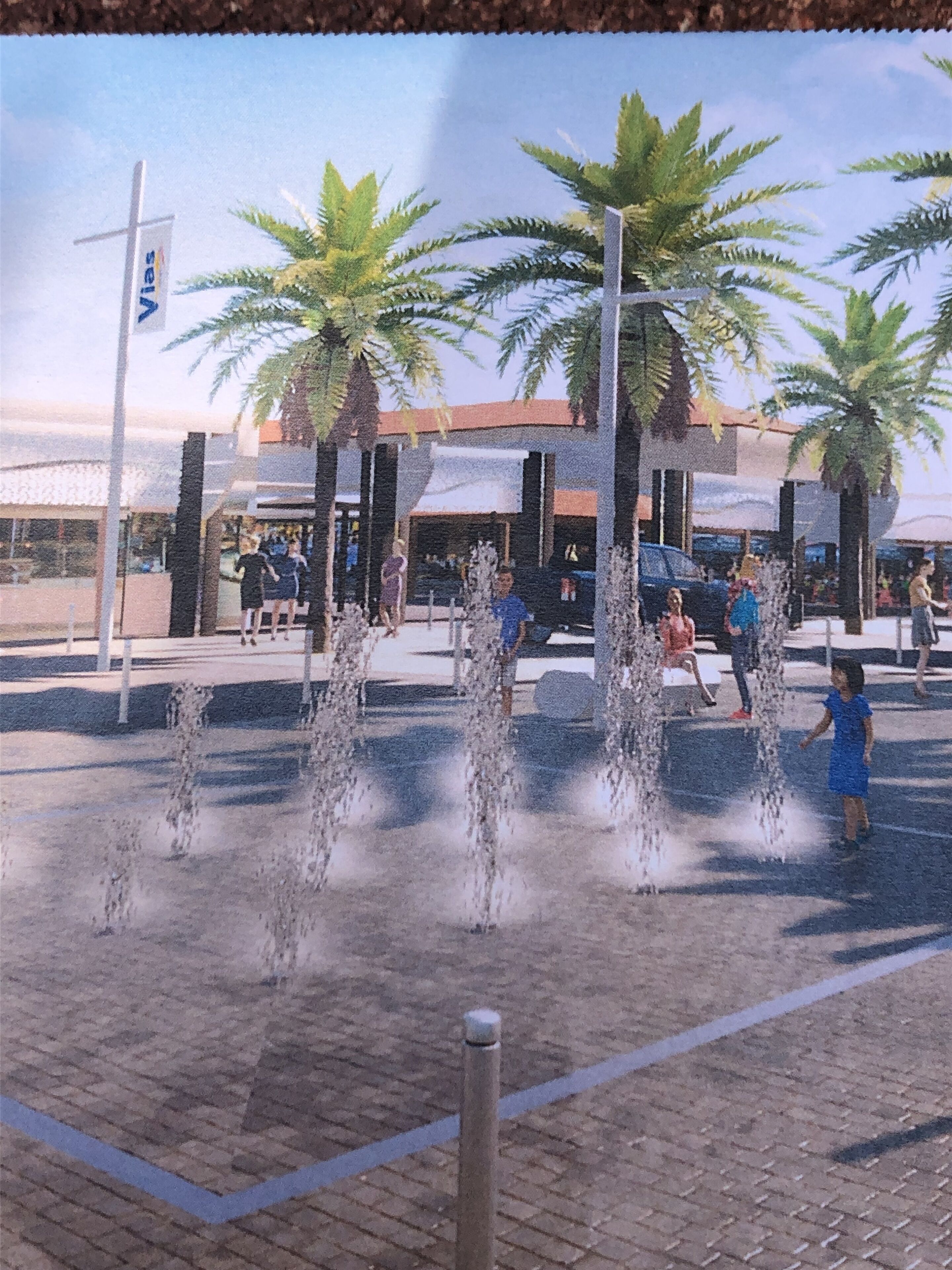 A public square with a water feature, palm trees, and people.