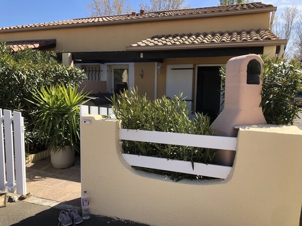 Una casa con fachada color beige, techo de tejas y un portón blanco.