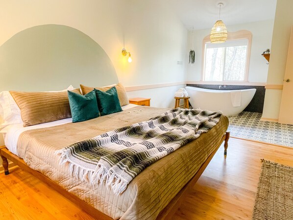 A bedroom with a bed, a nightstand, a window, and a bathtub.