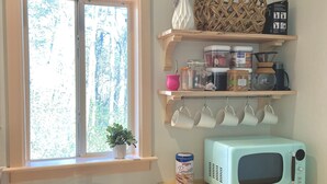 Una cocina con encimera de madera, un lavabo, una ventana con vistas a árboles, estantes con frascos y un microondas.