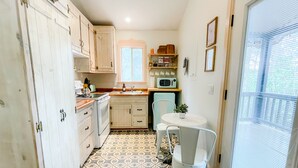 Cocina compacta con armarios blancos, microondas y un pequeño comedor con una silla y mesa.