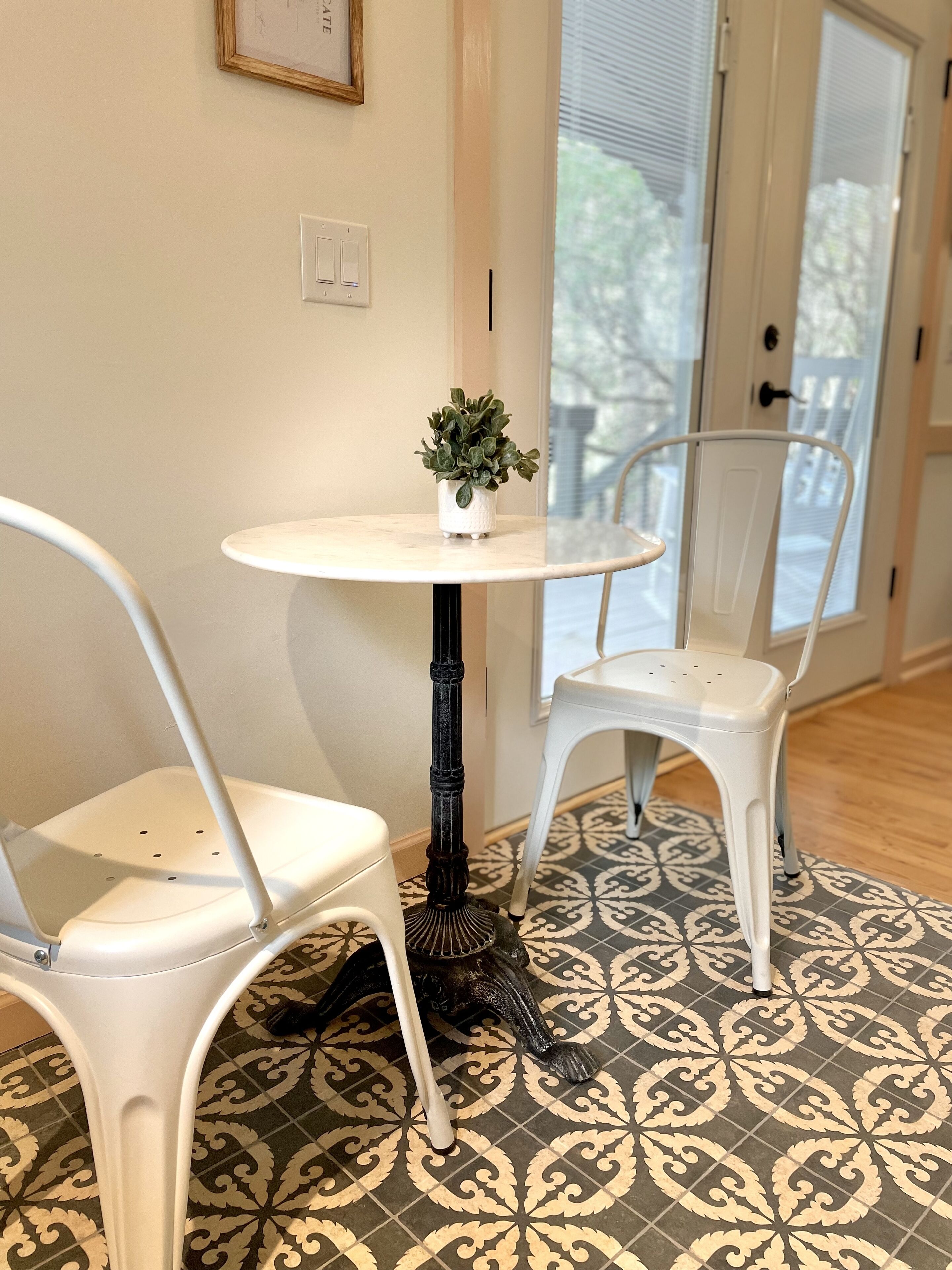 A small round table with a potted plant, two white chairs, and patterned floor tiles.