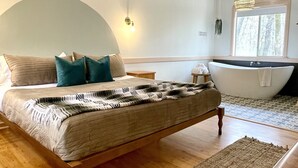 Un dormitorio con cama, bañera y un ventanal grande.