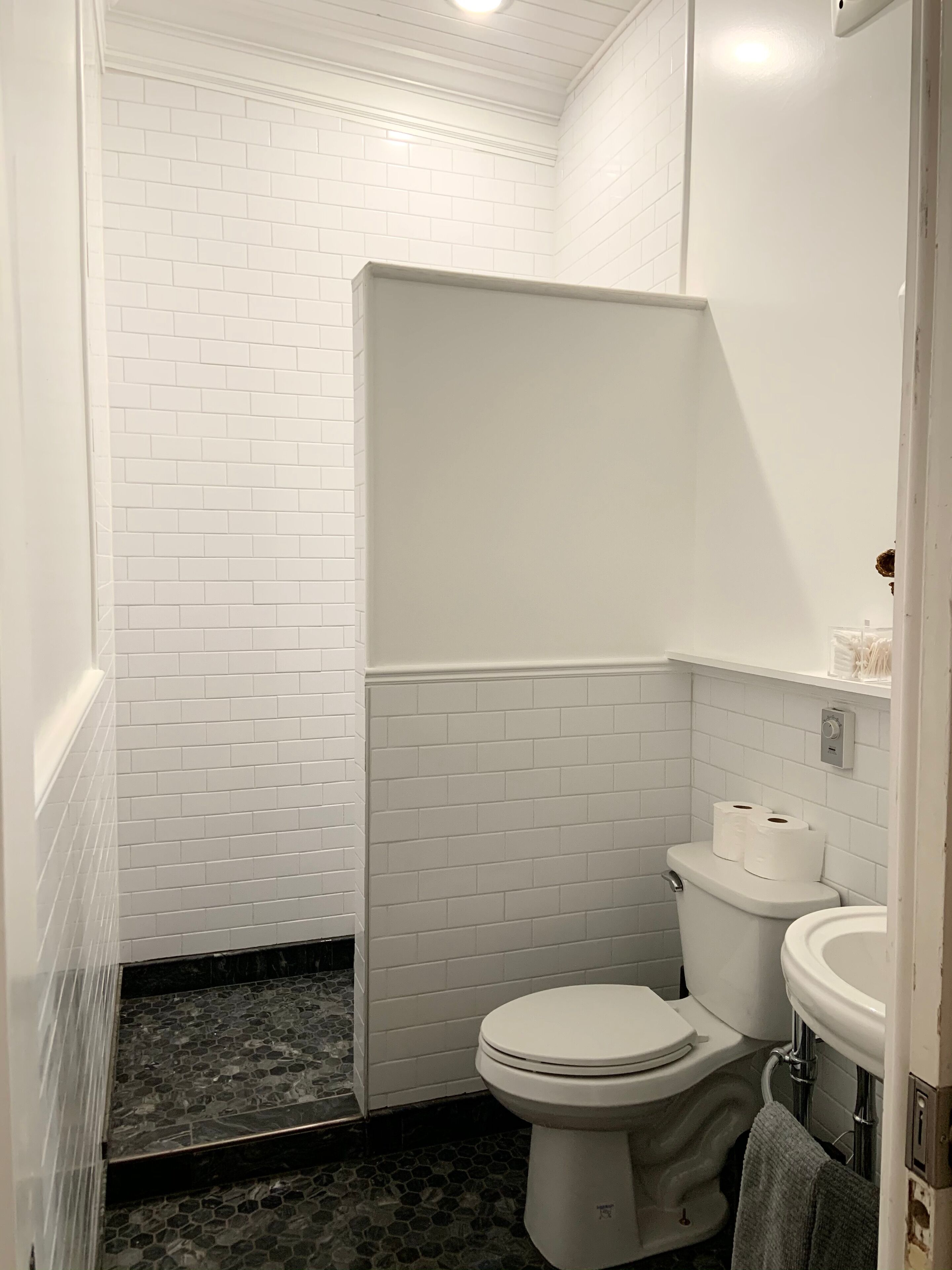 A bathroom with white subway tiles, a toilet, a sink, and a shower area.