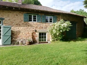 Una casa de piedra con techo de tejas, puerta verde y un pequeño jardín.