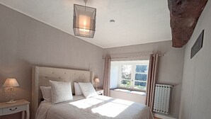 Une chambre à coucher avec un grand lit, une table de chevet, une lampe, une fenêtre avec des rideaux et un radiateur.