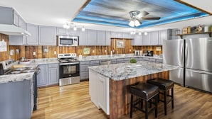 Een moderne keuken met granieten aanrechtbladen, roestvrijstalen apparatuur en een centraal kookeiland met barstoelen.