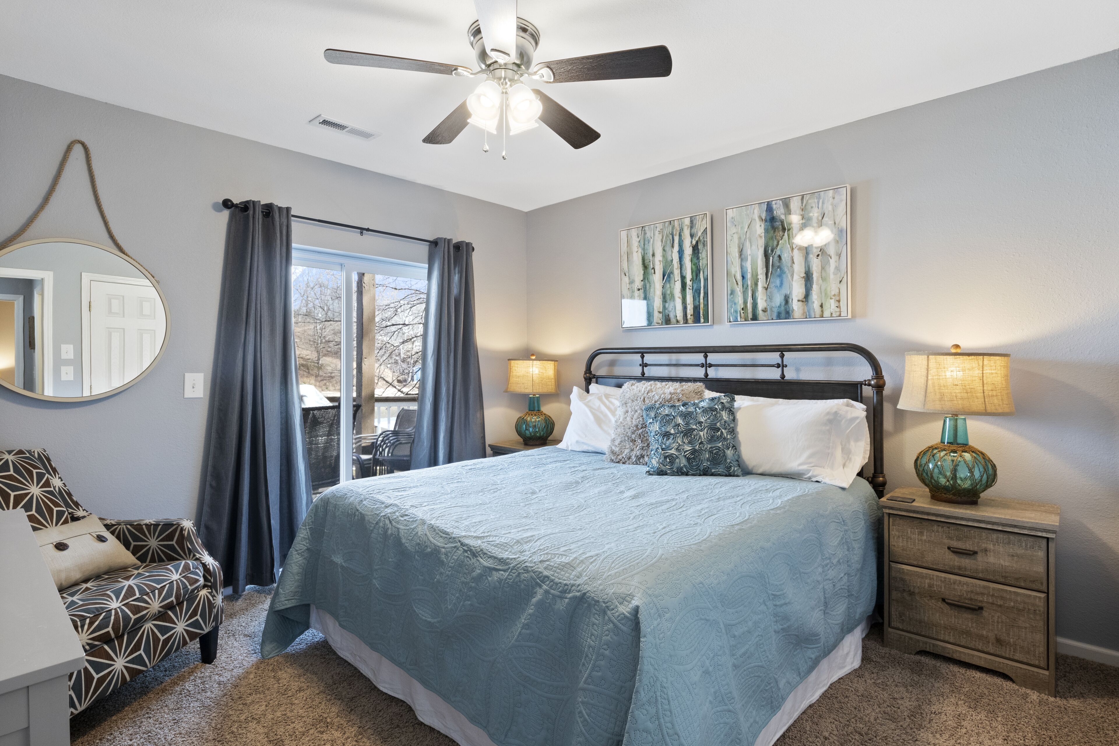 Une chambre à coucher comprenant un lit, deux tables de chevet avec des lampes, un ventilateur de plafond, une fenêtre avec des rideaux et une chaise.