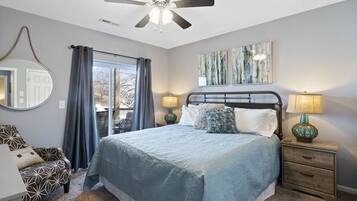 Une chambre à coucher comprenant un lit, deux tables de chevet avec des lampes, un ventilateur de plafond, une fenêtre avec des rideaux et une chaise.