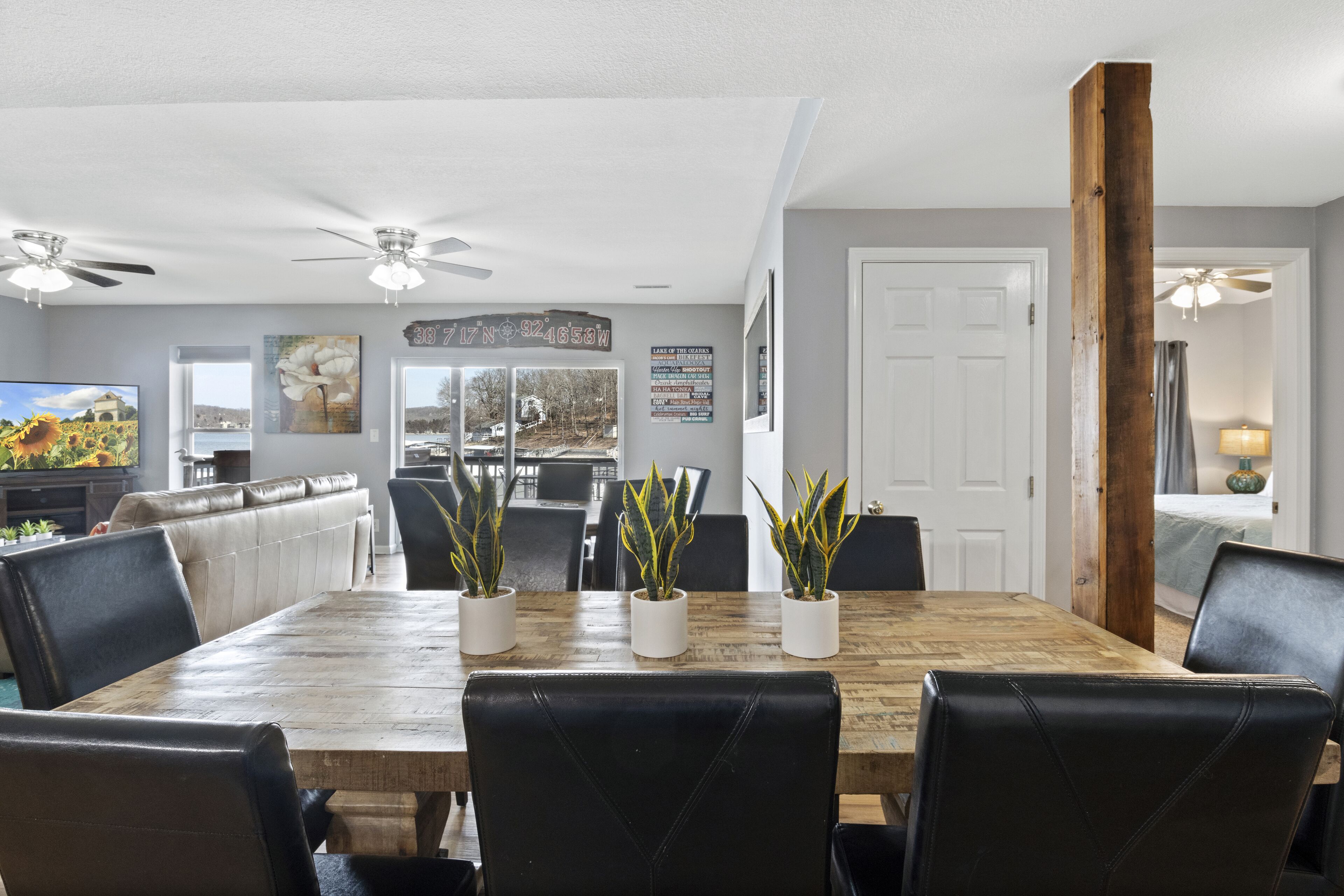 A dining area with a wooden table, black leather chairs, and potted plants.