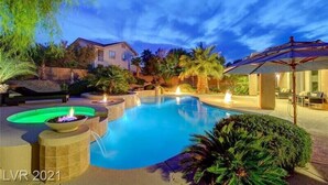 A swimming pool with a fire feature, surrounded by tropical plants and a covered patio area. - Spectacular custom home with private pool (Las Vegas)