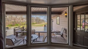 A bay window with a view of a deck, outdoor furniture, and a flag. - Lakefront Retreat with Dock and Fire Pit (Gilbertsville)
