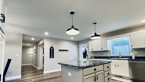A modern kitchen with a central island, white cabinetry, and pendant lighting. - Lakefront Retreat with Dock and Fire Pit (Gilbertsville)