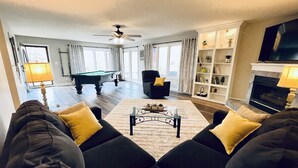 Een woonkamer met een pooltafel, een zithoek, een open haard en een televisie.