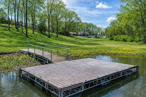 Eine Holzsteg erstreckt sich in ruhiges Wasser, umgeben von üppigem Grün und blauem Himmel.