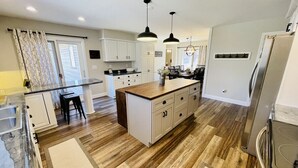 Een moderne keuken met houten vloeren, witte kasten, een centraal eiland en hangende lampen.