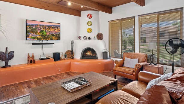A living room with a fireplace, leather furniture, a television, and a large window with blinds. - Fort Marcy 33 | Walk to Plaza | Kiva Fireplace | Full Kitchen | Hot Tub | Pool | Single Level (Santa Fe)