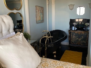 A luxurious bedroom with a large bed, a classic bathtub, and a vintage dresser.